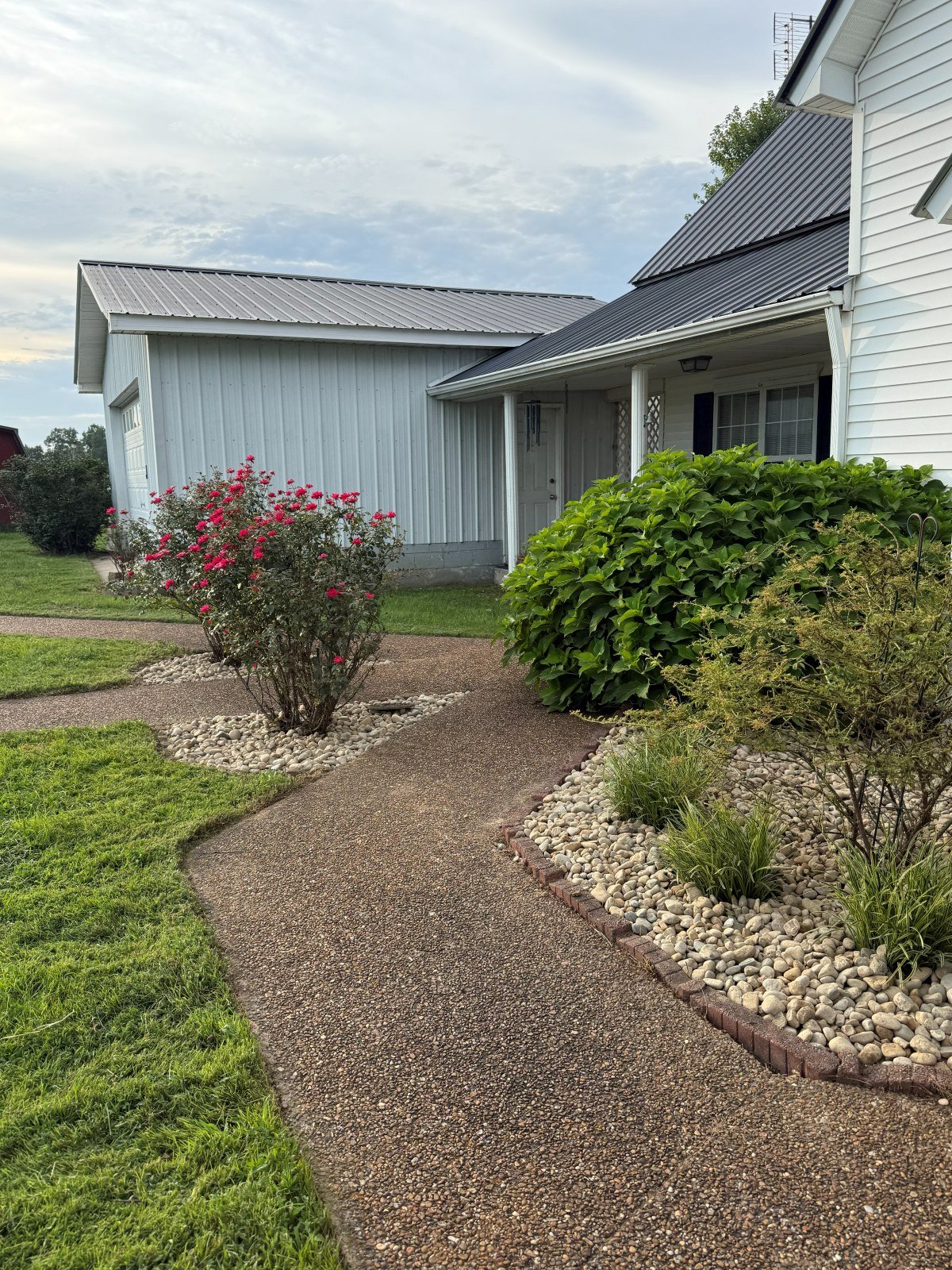 River rock landscape beds with blooming roses along a walkway